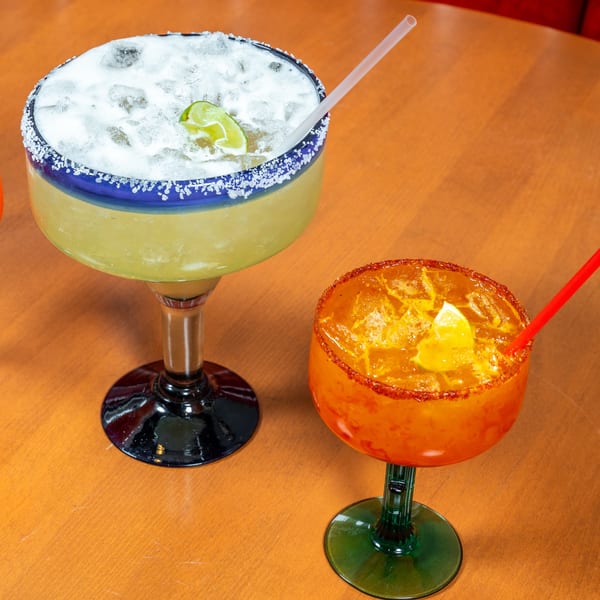 Two margaritas, one classic lime and one orange with chili rim, on a wooden table.