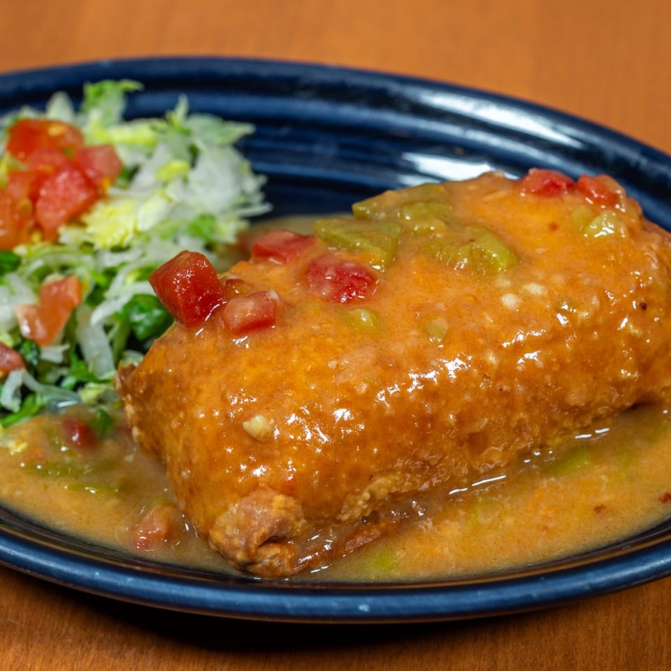 Mi Cocina's chimichanga covered in orange sauce with diced tomatoes and green peppers, served with lettuce.