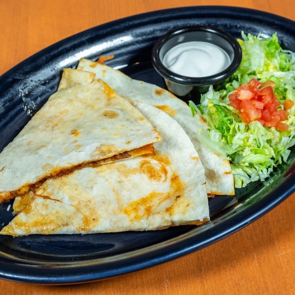 Three golden-brown quesadilla wedges with a side of shredded lettuce, diced tomatoes, and sour cream.