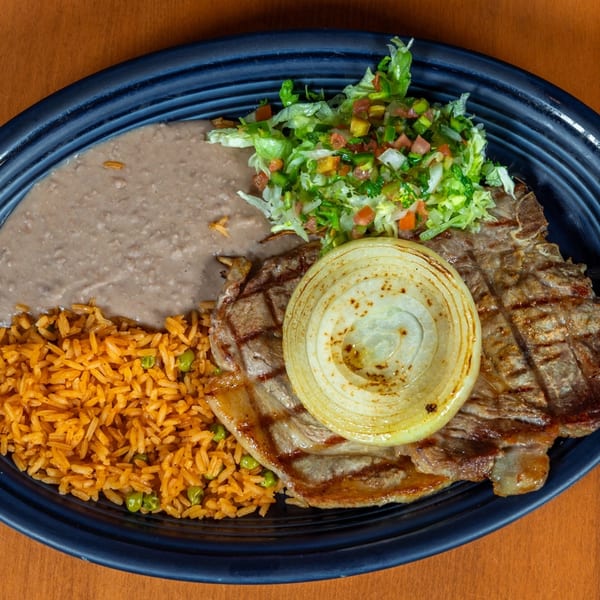 Mi Cocina's grilled steak with a large onion slice, refried beans, Mexican rice, and fresh pico de gallo.