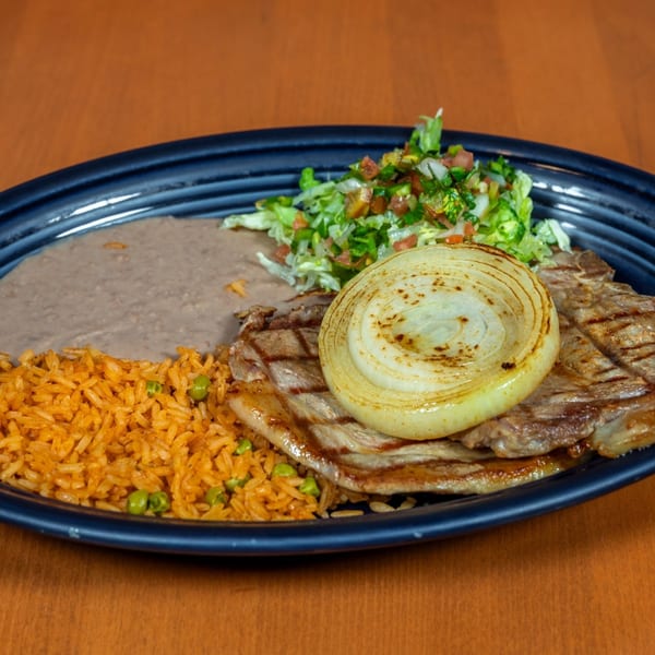 Grilled steak with a large onion slice, rice, refried beans, and a fresh salad on a dark plate.