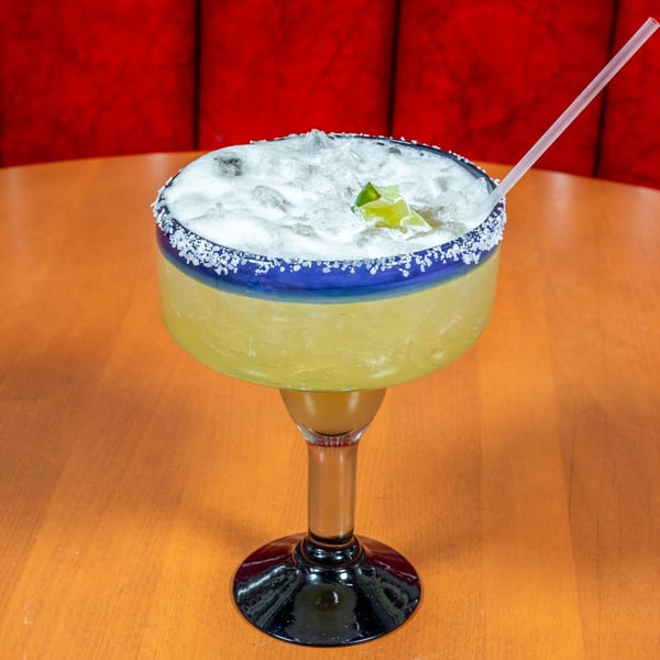 A large Mi Cocina margarita with ice, lime, and a salted rim on a wooden table.